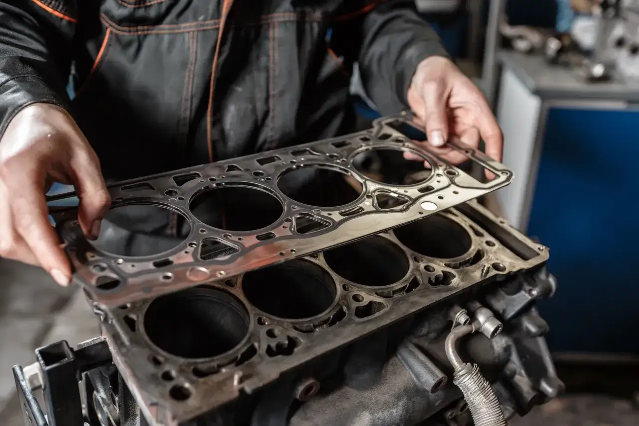 Mechanik trzyma nową uszczelkę pod głowicę, gotową do montażu. Zapobiega wyciekom płynu chłodniczego.