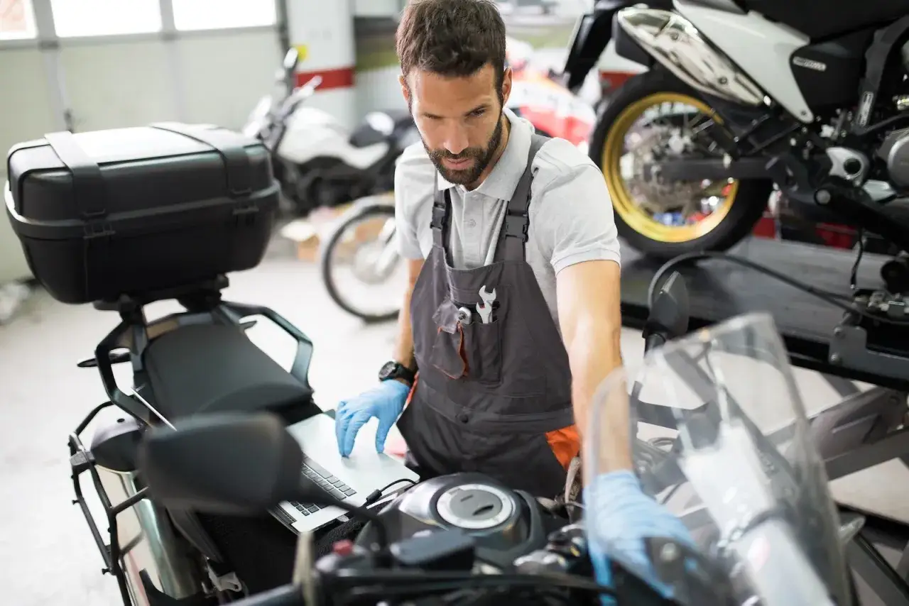 Mechanik w rękawiczkach sprawdza na laptopie przegląd motocykla po terminie.