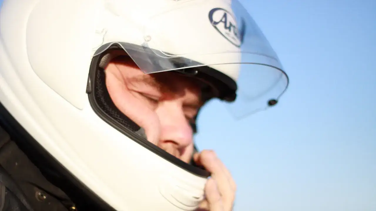 Mężczyzna w białym, integralnym kasku motocyklowym z podniesioną szybką, przygotowuje się do jazdy.
