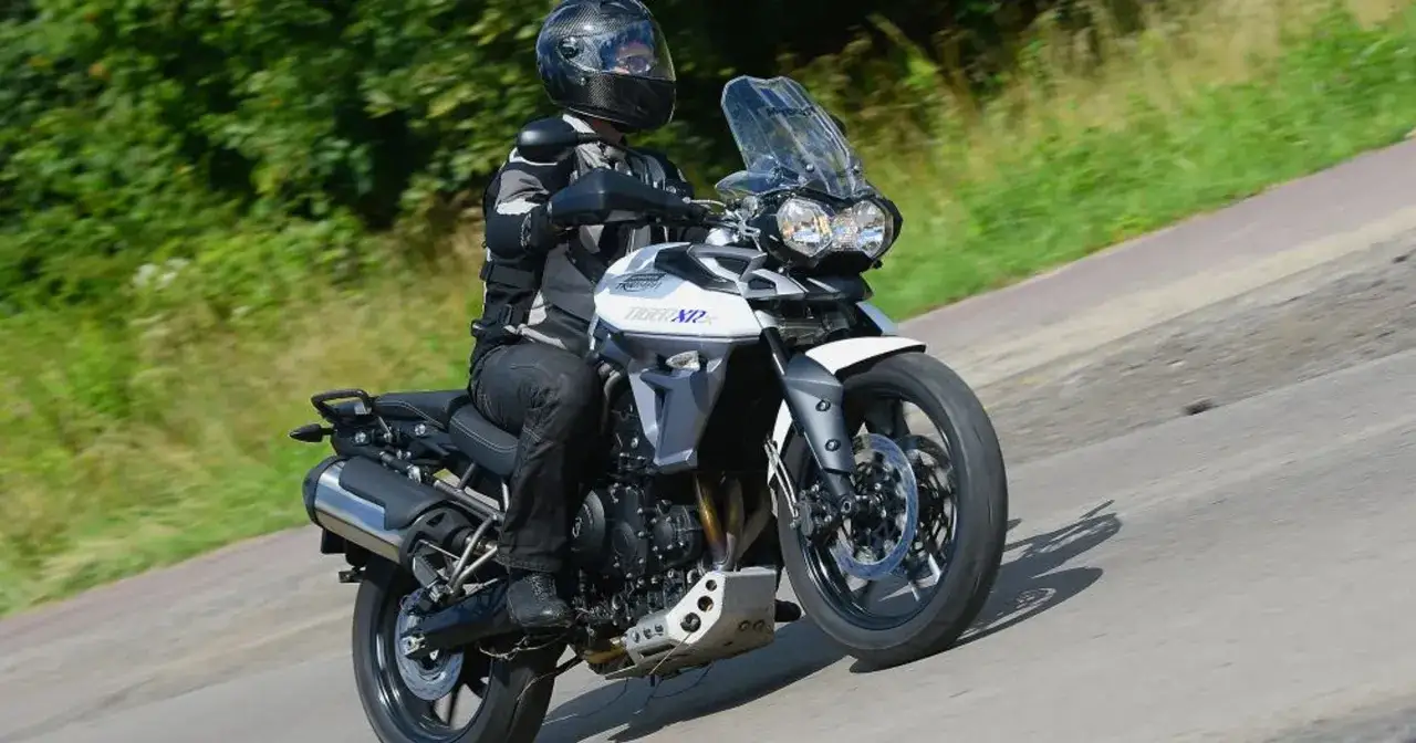 Motocyklista w kasku jedzie motocyklem Triumph Tiger 800 XRX Low po drodze wśród zieleni.