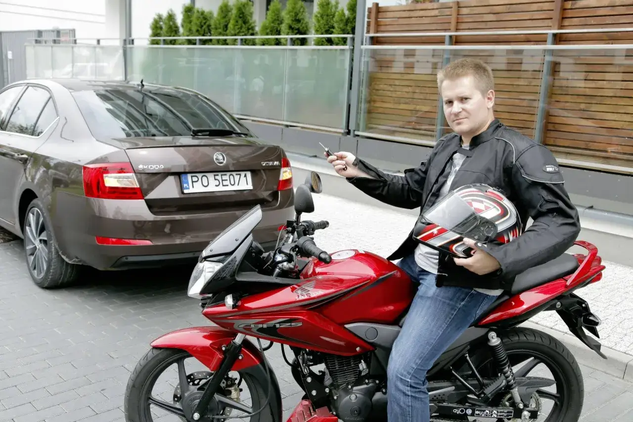 Mężczyzna na czerwonym motocyklu trzyma kluczyki. Czy prawo jazdy kat B uprawnia do kierowania motorowerem?