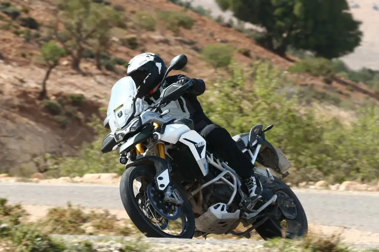 Motocyklista na motocyklu Tiger 900 GT Pro pokonuje zakręt na górskiej drodze.