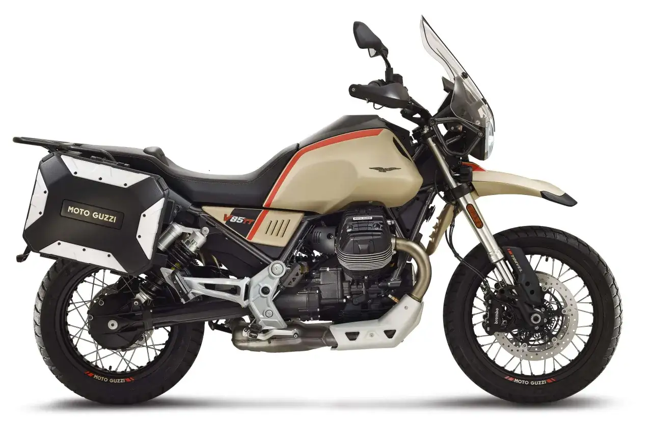 Beżowy motocykl Moto Guzzi V85 TT z czarnymi kuframi i czerwonymi akcentami, gotowy na przygodę.