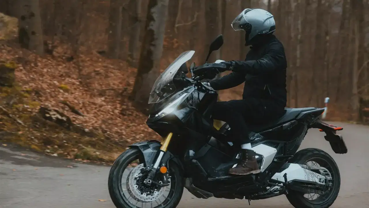 Motocyklista w kasku jedzie na skuterze Honda X-ADV 750 przez jesienny las.