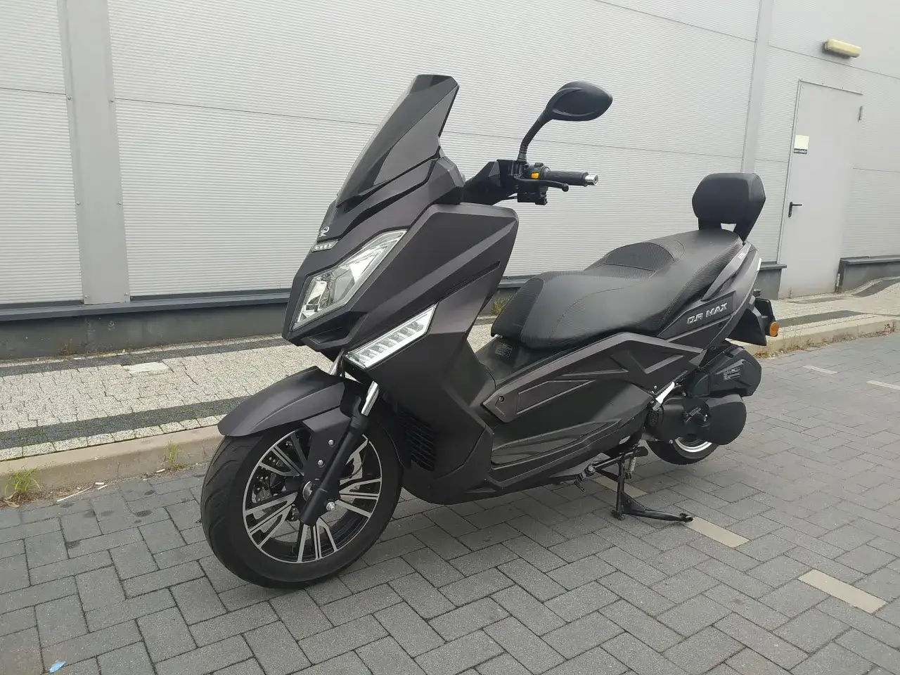 Czarny skuter Zipp QR Max 125 stoi na chodniku przed budynkiem.