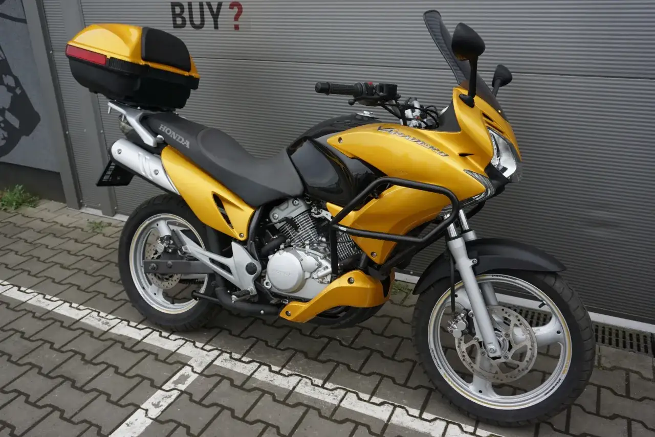Złoty motocykl Honda Varadero 125, gotowy na odblokowanie mocy. Z kuferkiem na bagaż i osłoną silnika.