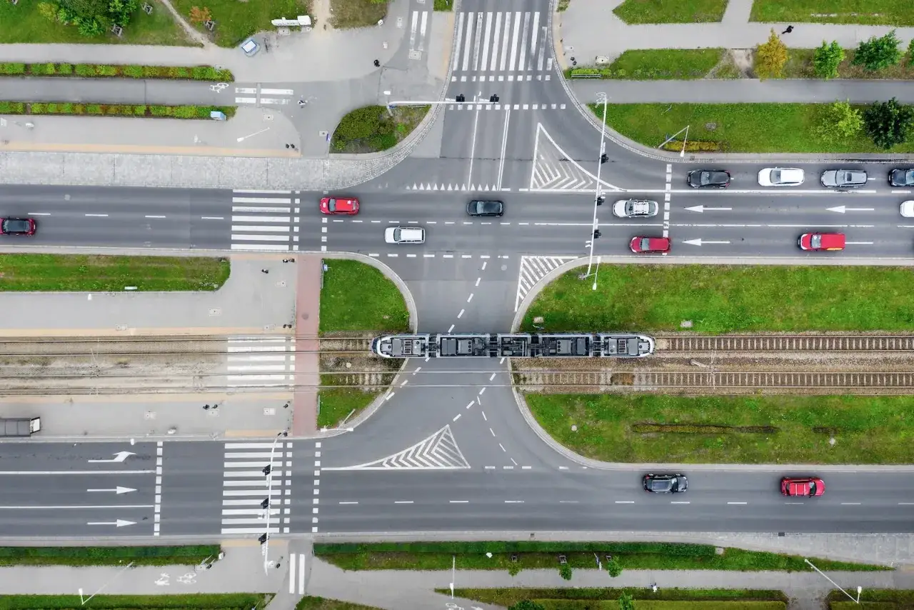 Widok z góry na skrzyżowanie z tramwajem i samochodami. Widać pasy ruchu, przejścia dla pieszych i zielone tereny. W jakiej odległości od skrzyżowania można parkować?