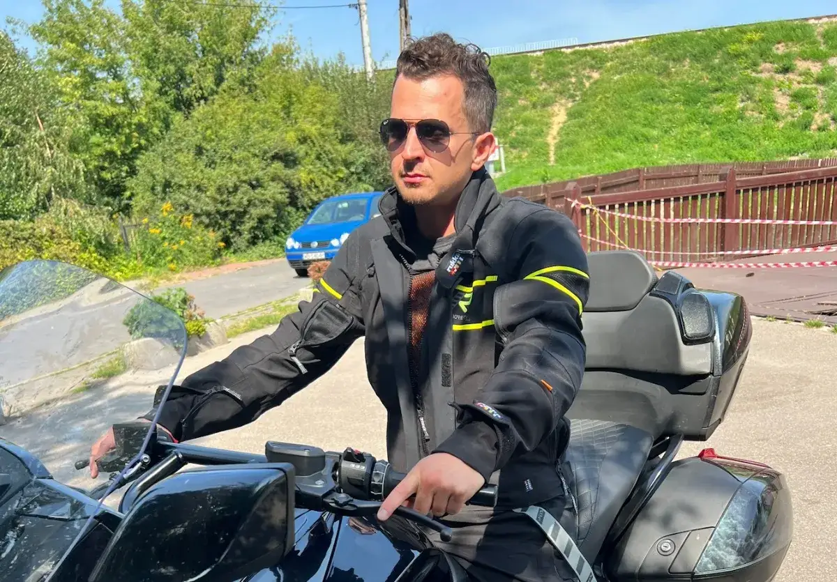 Mężczyzna w okularach przeciwsłonecznych i czarnym ubraniu na motor turystyczny, gotowy do podróży.