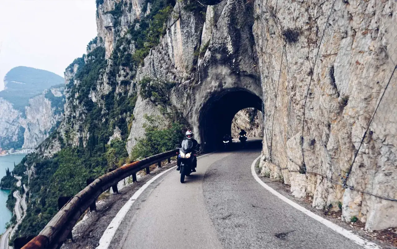 Motocykliści przemierzają malowniczą Strada della Forra, wjeżdżając w skalny tunel.