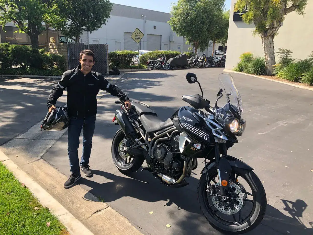 Uśmiechnięty motocyklista z kaskiem w ręku obok czarnego motocykla Triumph Tiger 800 XRX Low.