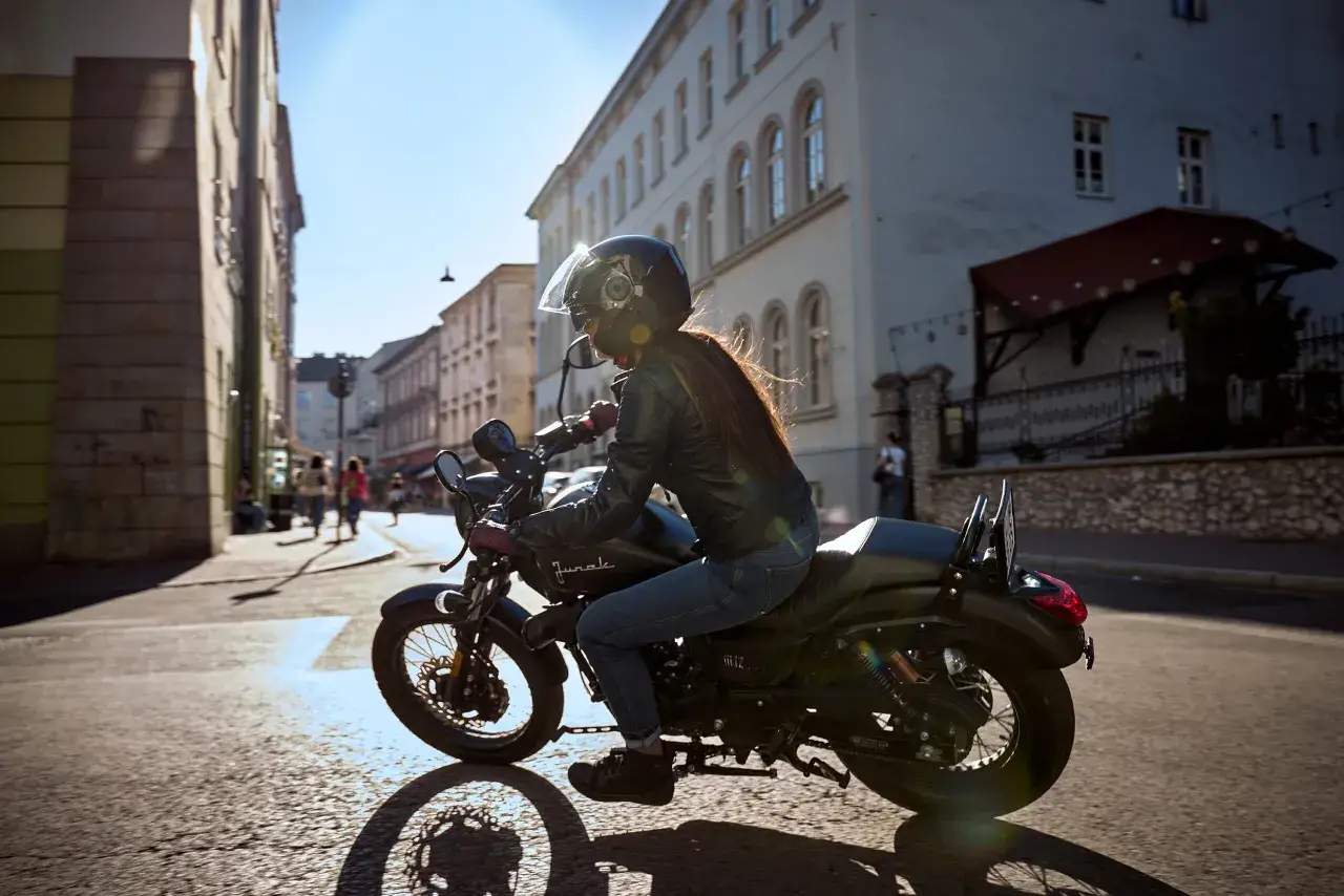 Kobieta w kasku i skórzanej kurtce jedzie motocyklem po mieście. Zastanawiasz się, ile pali motocykl?