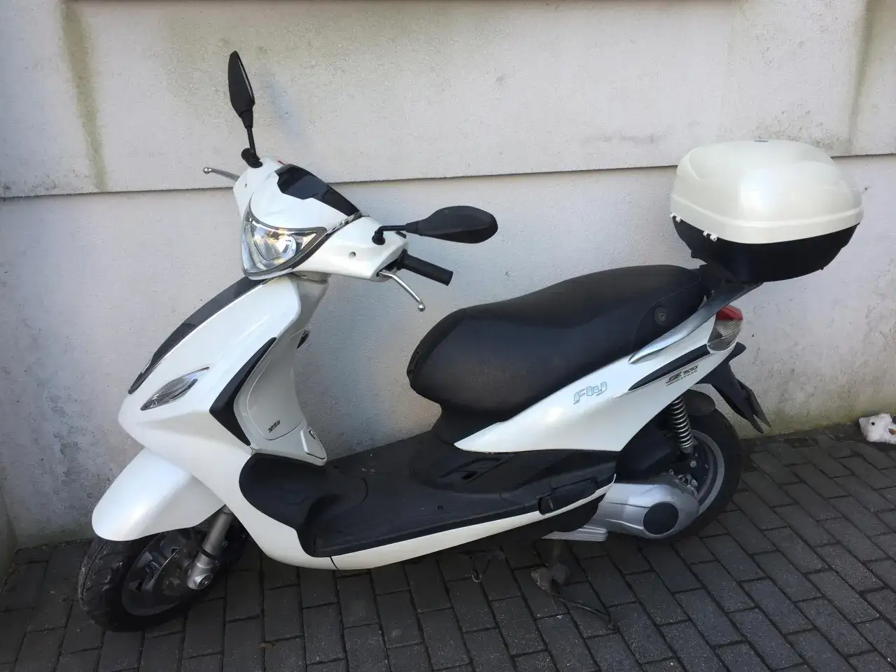 Biały skuter Piaggio Fly 125 z czarnym siedzeniem i kufrem. Poznaj piaggio fly 125 dane techniczne.