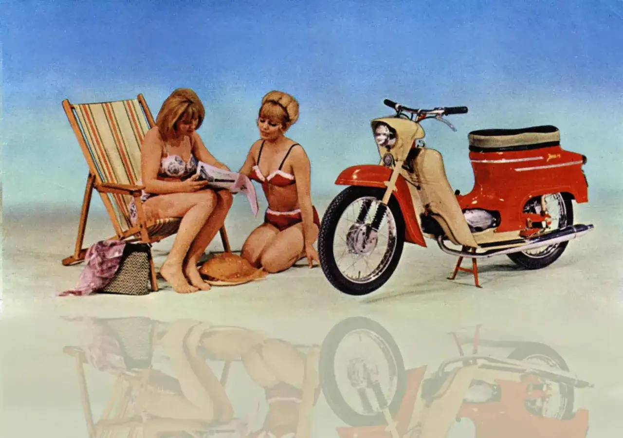 Dwie dziewczyny w bikini odpoczywają przy plażowym leżaku i kultowym motorowerze Jawa 50 typ 20.