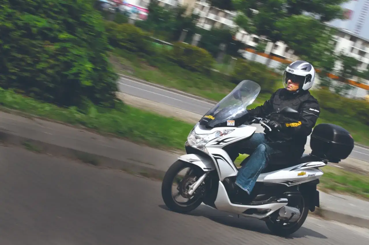 Biały skuter Honda PCX 125 w ruchu. Kierowca w kasku i kurtce jedzie po drodze. Dane techniczne tego modelu są imponujące.