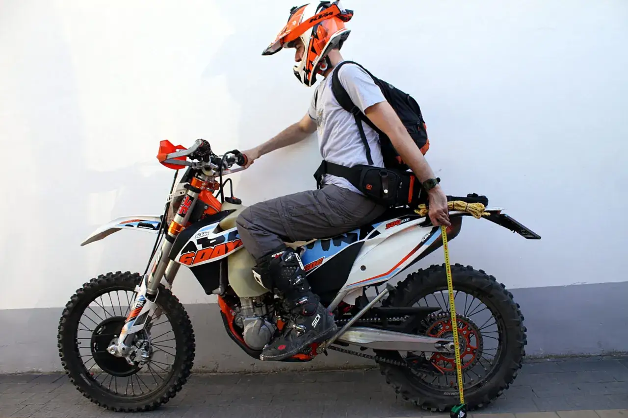 Mężczyzna w kasku mierzy ustawienie sag w motocyklu KTM 500 EXC.