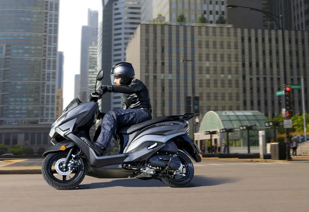 Mężczyzna w kasku i skórzanej kurtce jedzie na skuterze Suzuki Burgman 125 po mieście. Poznaj suzuki burgman 125 dane techniczne.