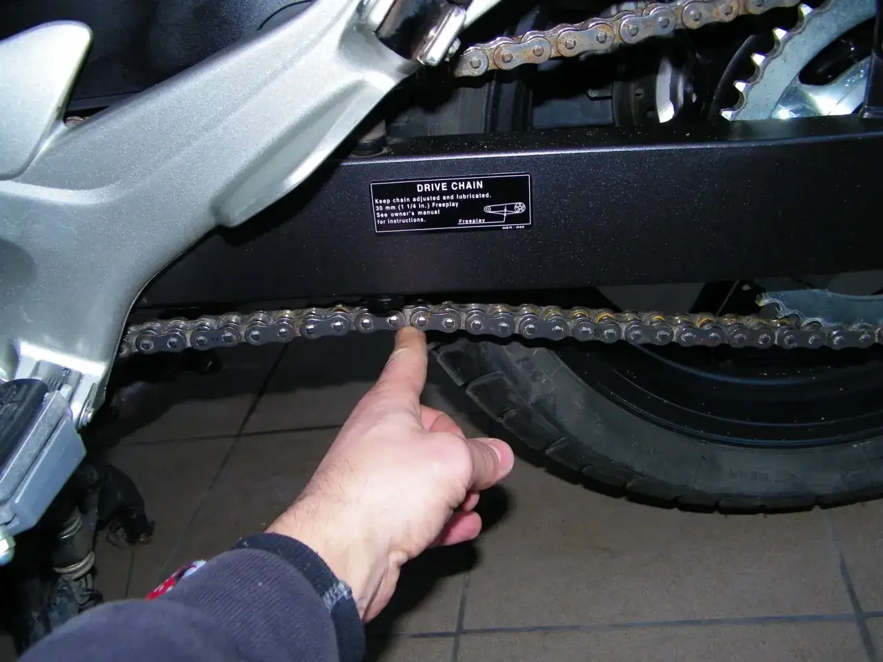 Palec pokazuje ogniwo łańcucha motocyklowego, ilustrując jak liczyć ogniwa w łańcuchu motocyklowym.