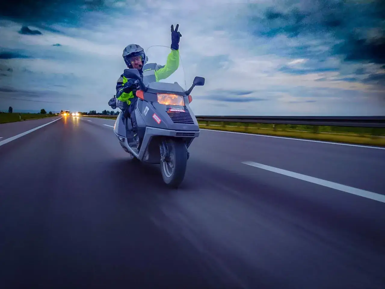 Motocyklista na skuterze 125 pozdrawia z autostrady, pokazując, że można nim jeździć po autostradzie.