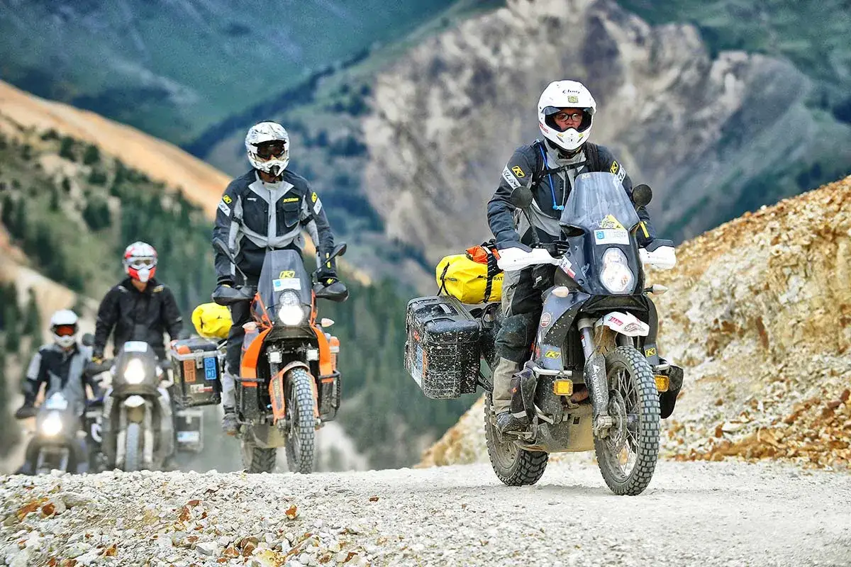 Motocykliści w kaskach i odzieży ochronnej jadący po kamienistej drodze w górach. Jaki przebieg dla motocykla jest duży? Taki, który pozwala na takie przygody.