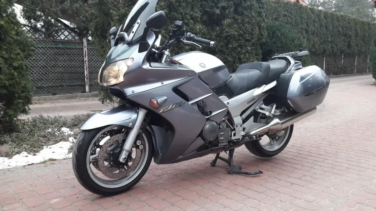 Srebrny motocykl Yamaha FJR 1300 na bruku, z widocznymi kuframi. Wady tego modelu to m.in. wysoka cena i waga.