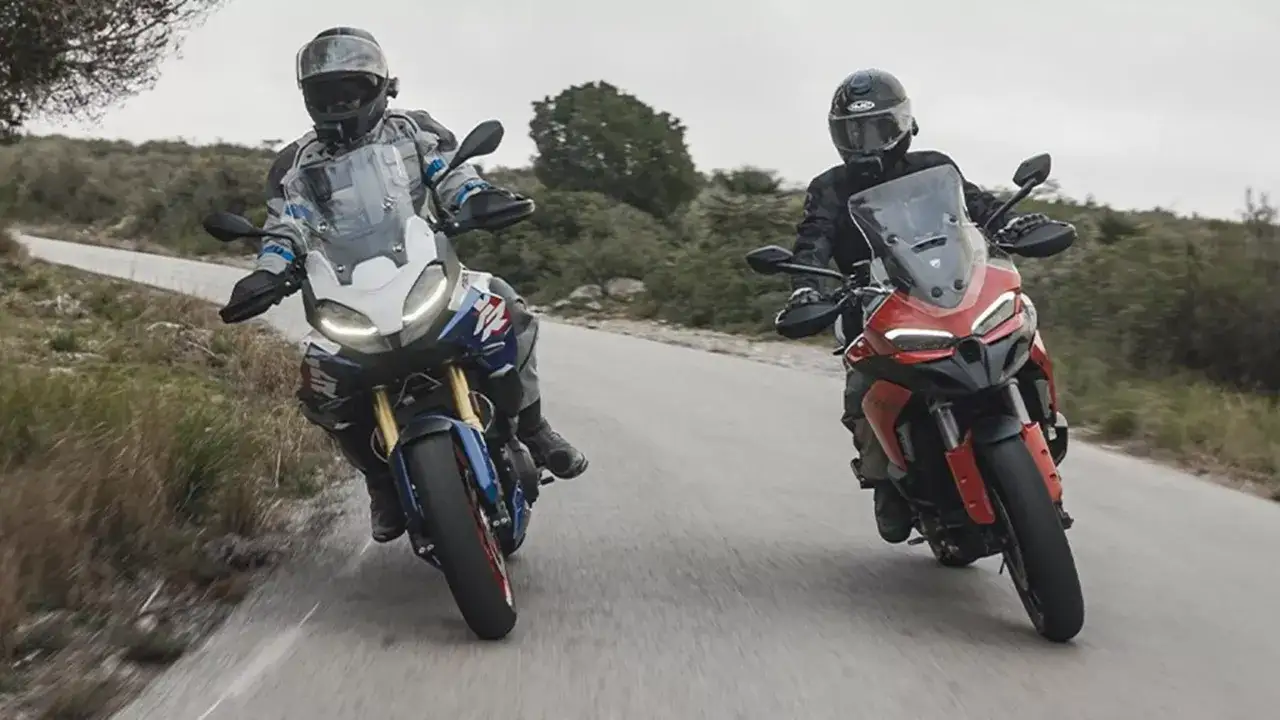 Dwóch motocyklistów na motocyklach Ducati Multistrada V2 przemierza krętą drogę wśród zieleni.