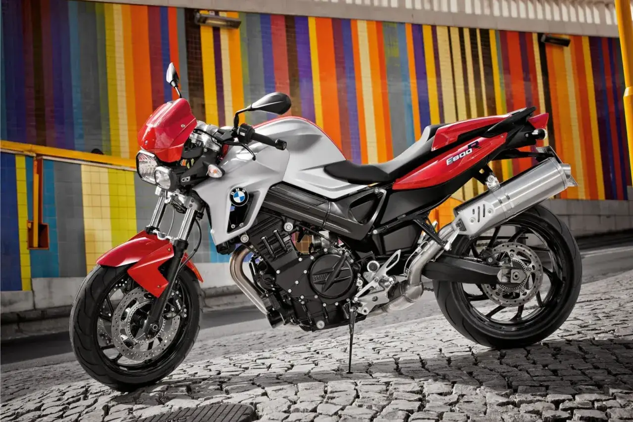BMW F800R dane techniczne: sportowy motocykl w kolorze srebrno-czerwonym, zaparkowany na brukowanej ulicy, na tle kolorowej ściany.