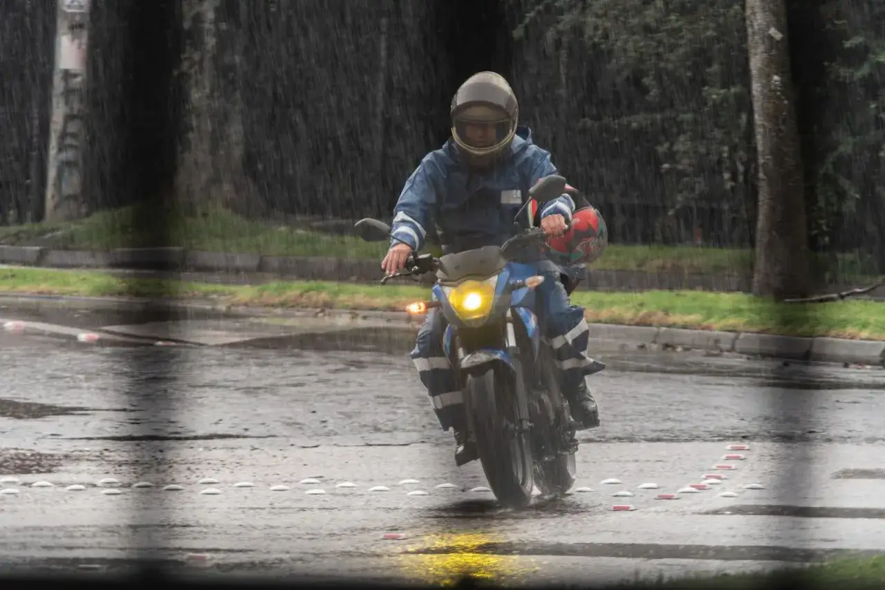 Motocyklista w niebieskim kombinezonie i kasku przemierza mokrą drogę. Jazda motocyklem w deszczu wymaga skupienia.