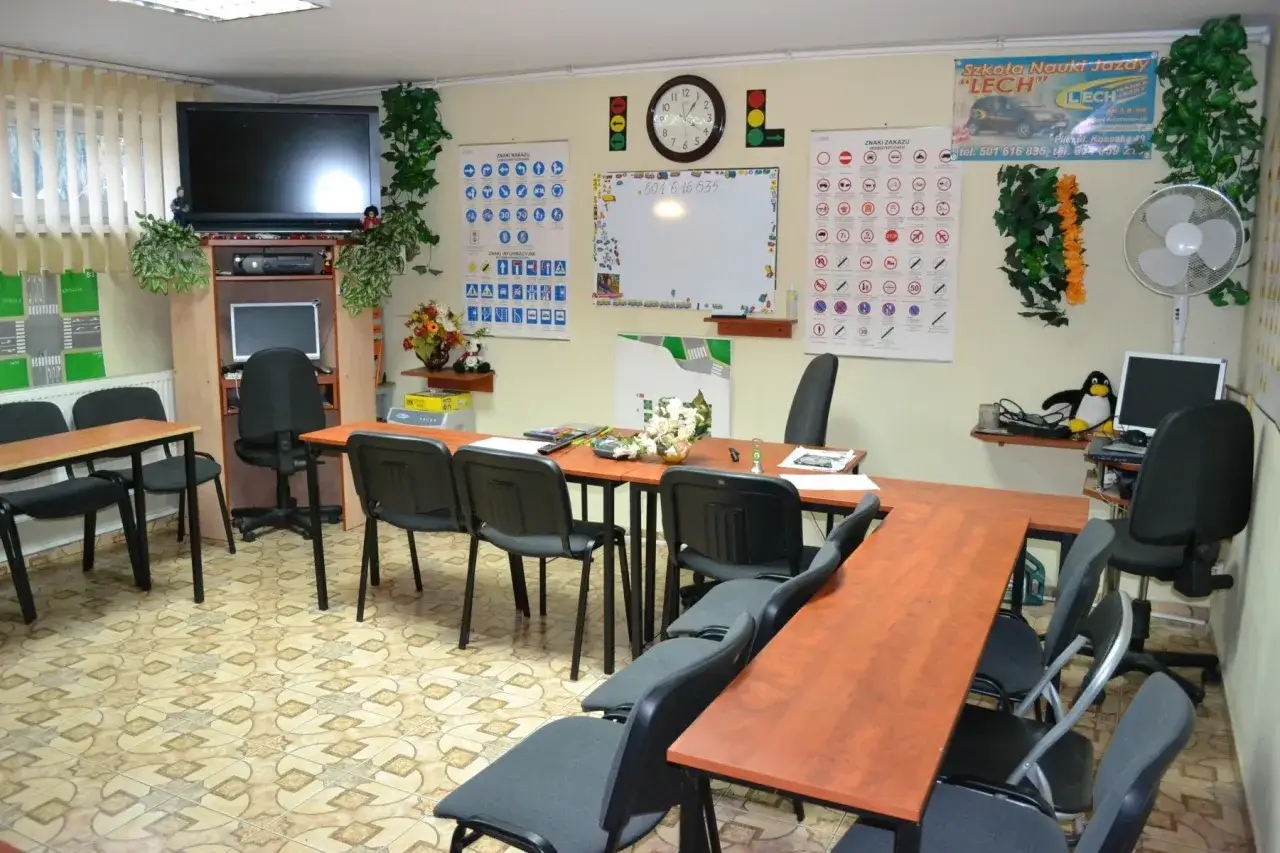 Sala wykładowa szkoły jazdy z tablicami znaków drogowych, zegarem i komputerem. Tu dowiesz się, ile trwa teoria na prawo jazdy.