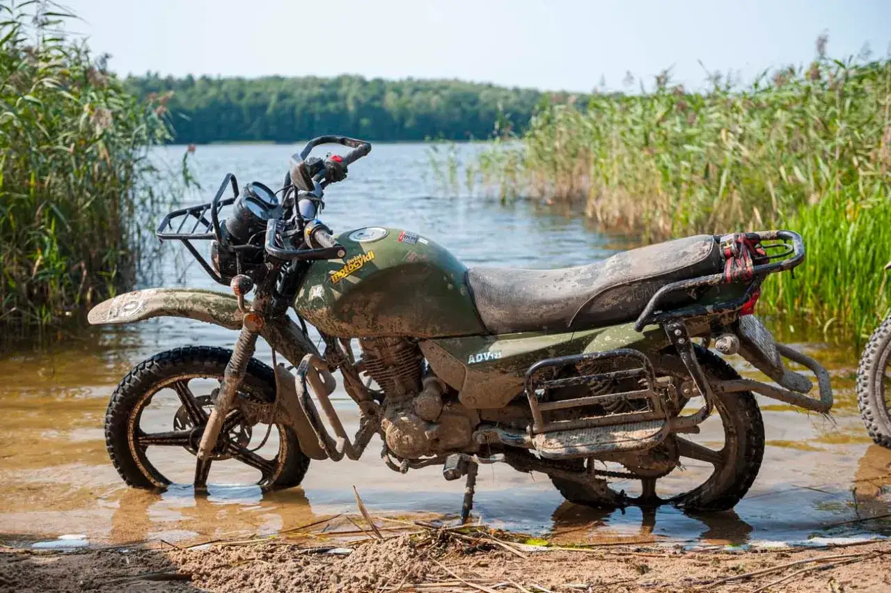Błotnisty motocykl ADV125 stoi w wodzie przy brzegu jeziora. To idealny sprzęt na wyprawę motocyklem dookoła Polski.