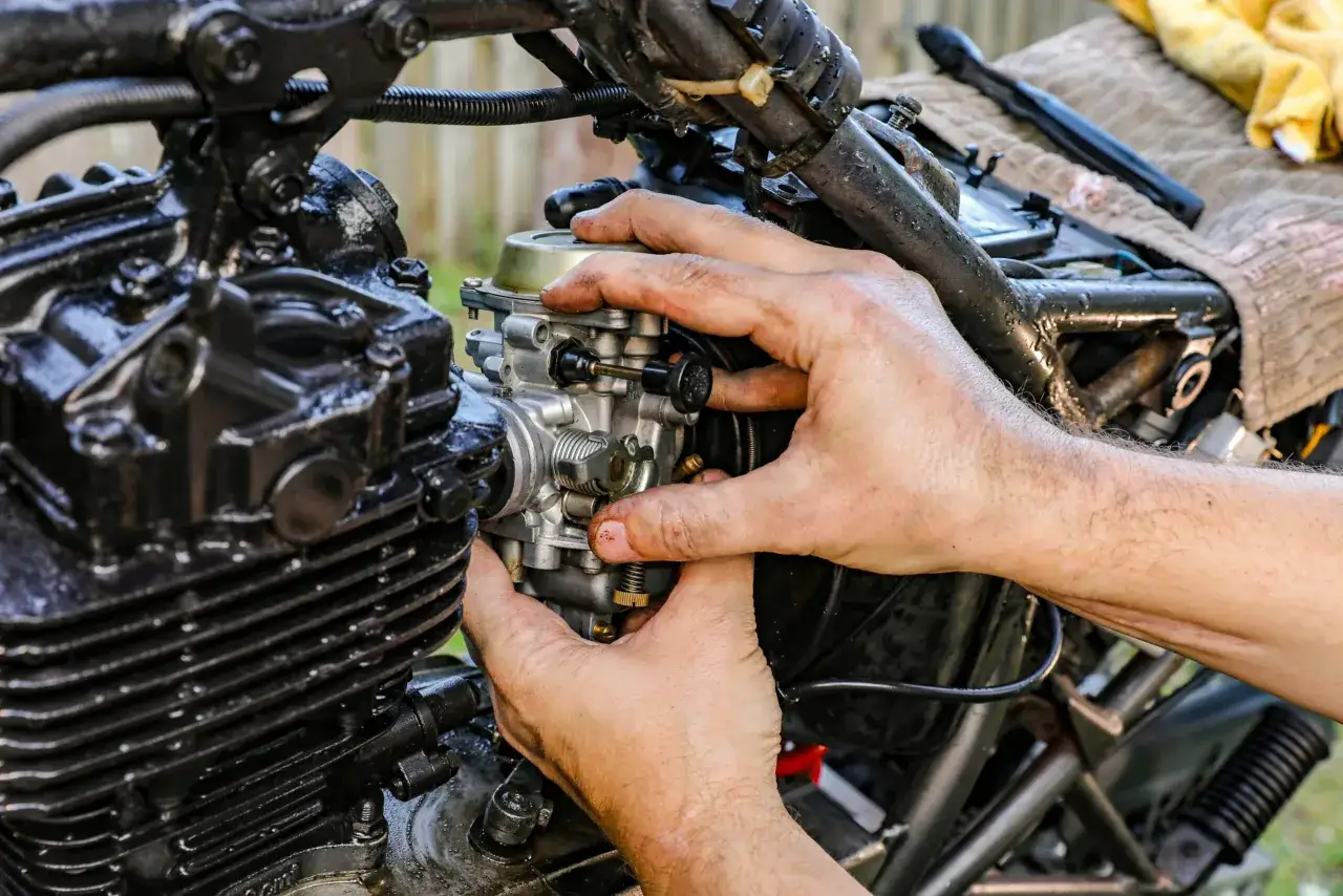 Dłonie majsterkowicza montują gaźnik motocykla, gdy ssanie jest włączone.