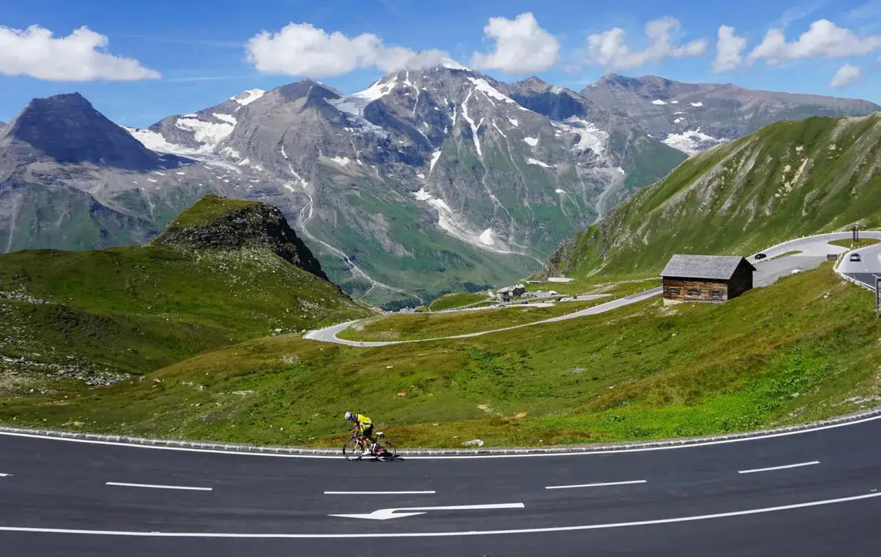Rowerzysta na tle alpejskich szczytów i serpentynowych tras motocyklowych w Austrii.