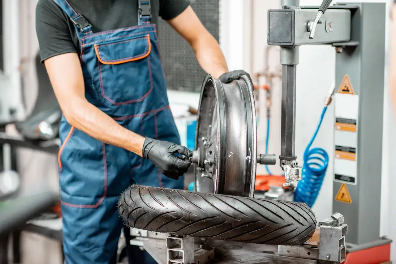 Mechanik w niebieskim kombinezonie dokonuje wymiany opony w skuterze, używając specjalistycznego sprzętu.