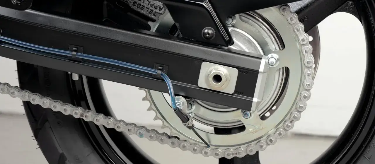 System automatycznego smarowania łańcucha motocykla, z niebieskim przewodem doprowadzającym smar do napędu.