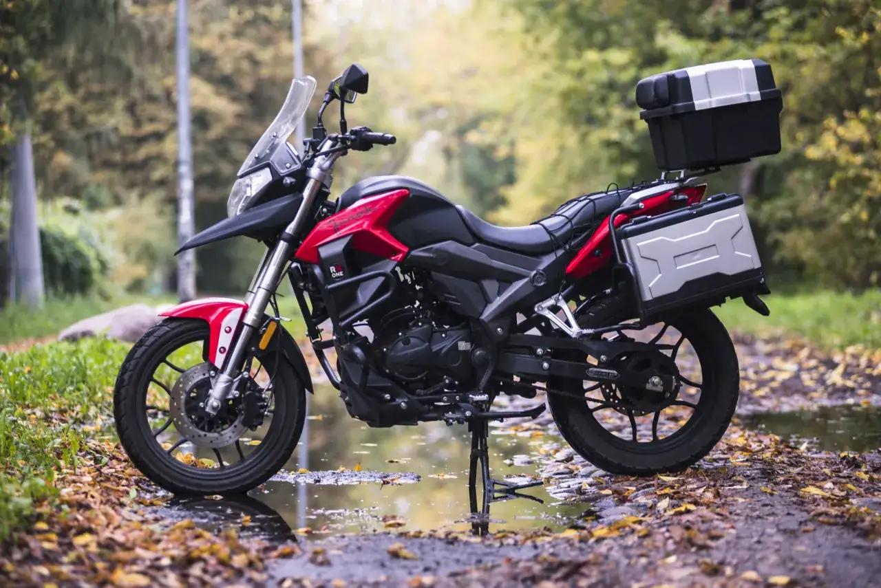 Czerwono-czarny motocykl 125 na postoju, gotowy do docierania. Jesienne liście i kałuże tworzą malownicze tło.