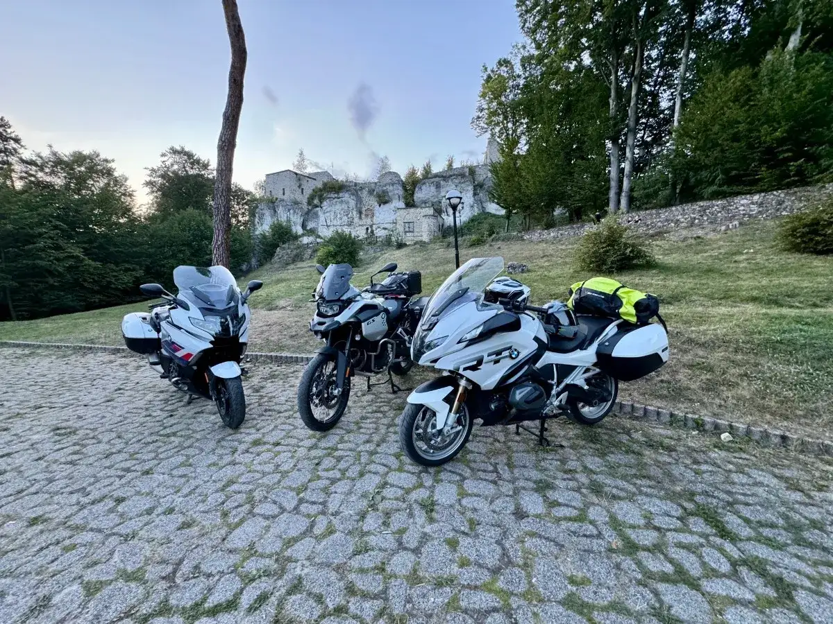 Trzy motocykle BMW gotowe na trasę motocyklową po Śląsku. W tle ruiny zamku i zielone drzewa.