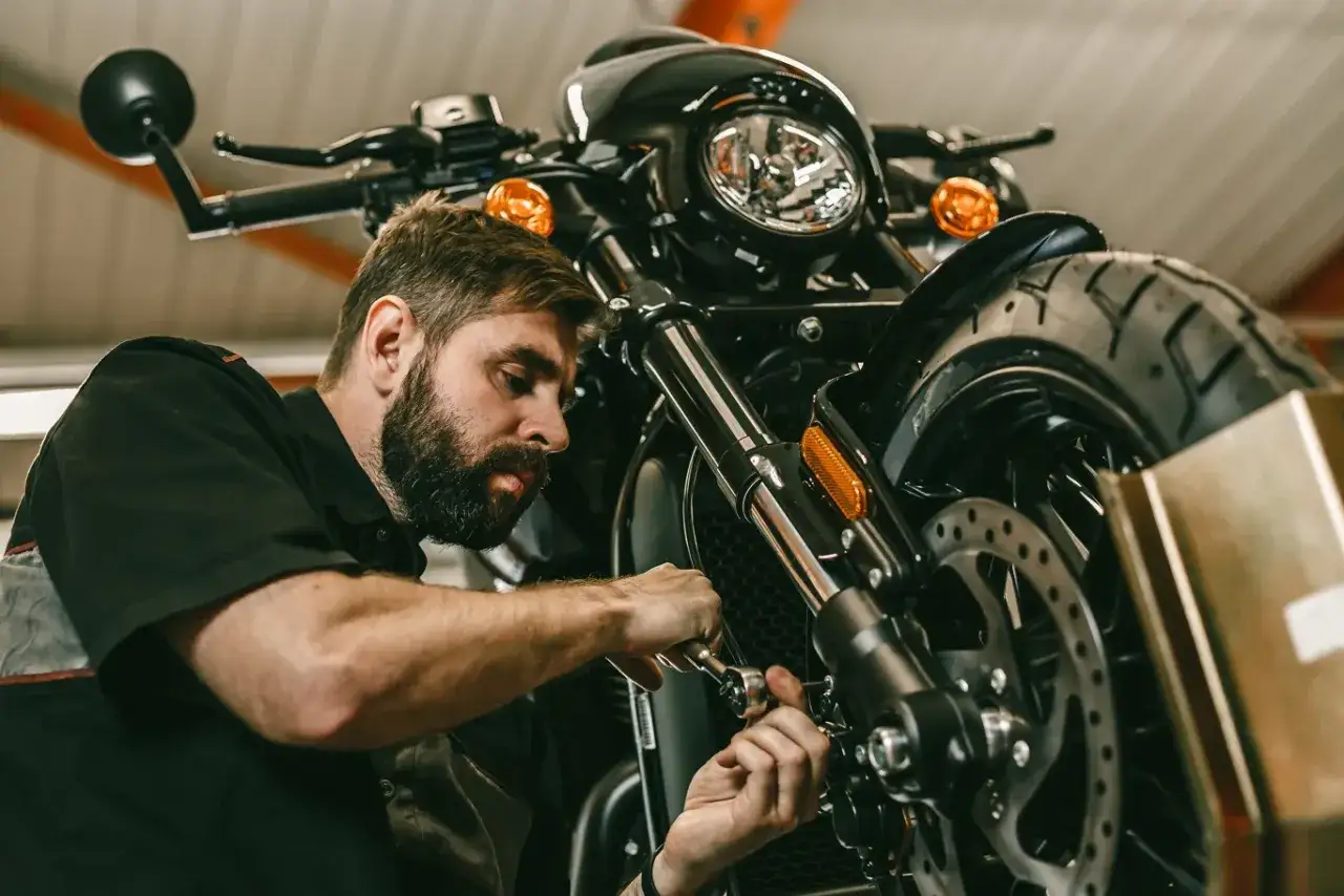Mechanik z brodą pracuje przy motocyklu. Rozrusznik kręci, a motocykl nie odpala.