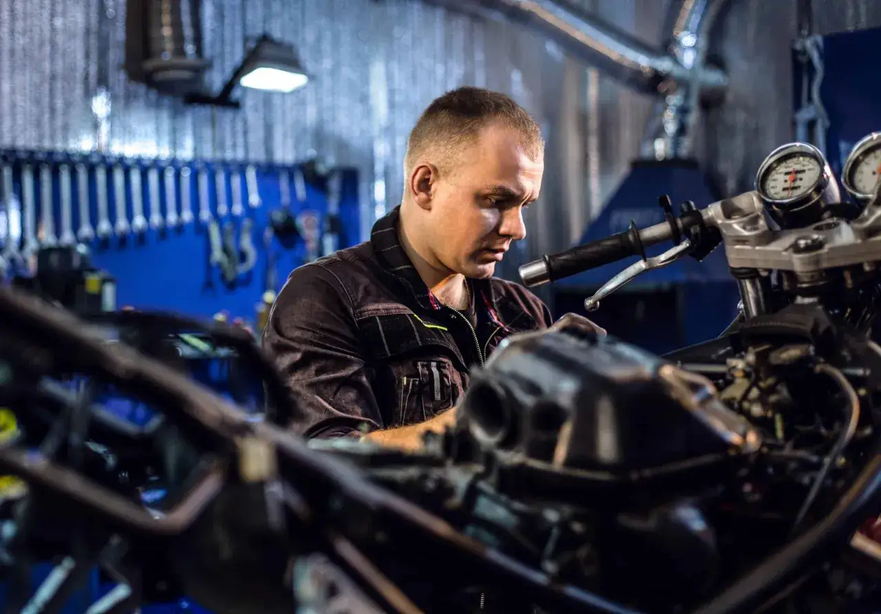Mechanik pracuje przy motocyklu, zastanawiając się, czy Castrol to dobry olej. W tle wiszą klucze.