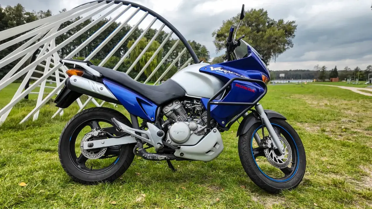 Honda Varadero 125, gotowy do odblokowania mocy. Motocykl stoi na trawie obok białej, metalowej konstrukcji.