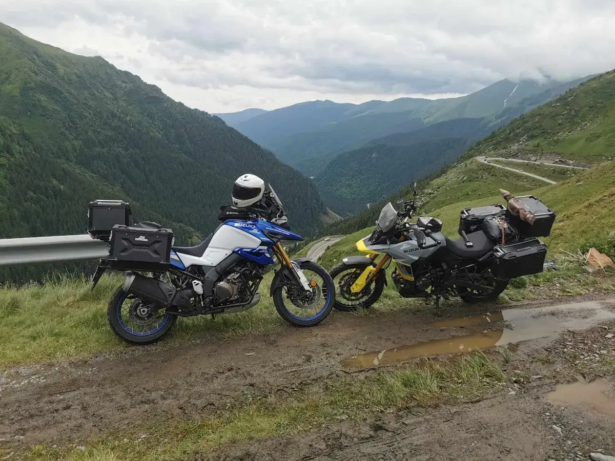 Dwa motocykle turystyczne na błotnistej drodze w g&oacute;rach. W tle kręta trasa motocyklowa Rumunia i zielone zbocza.