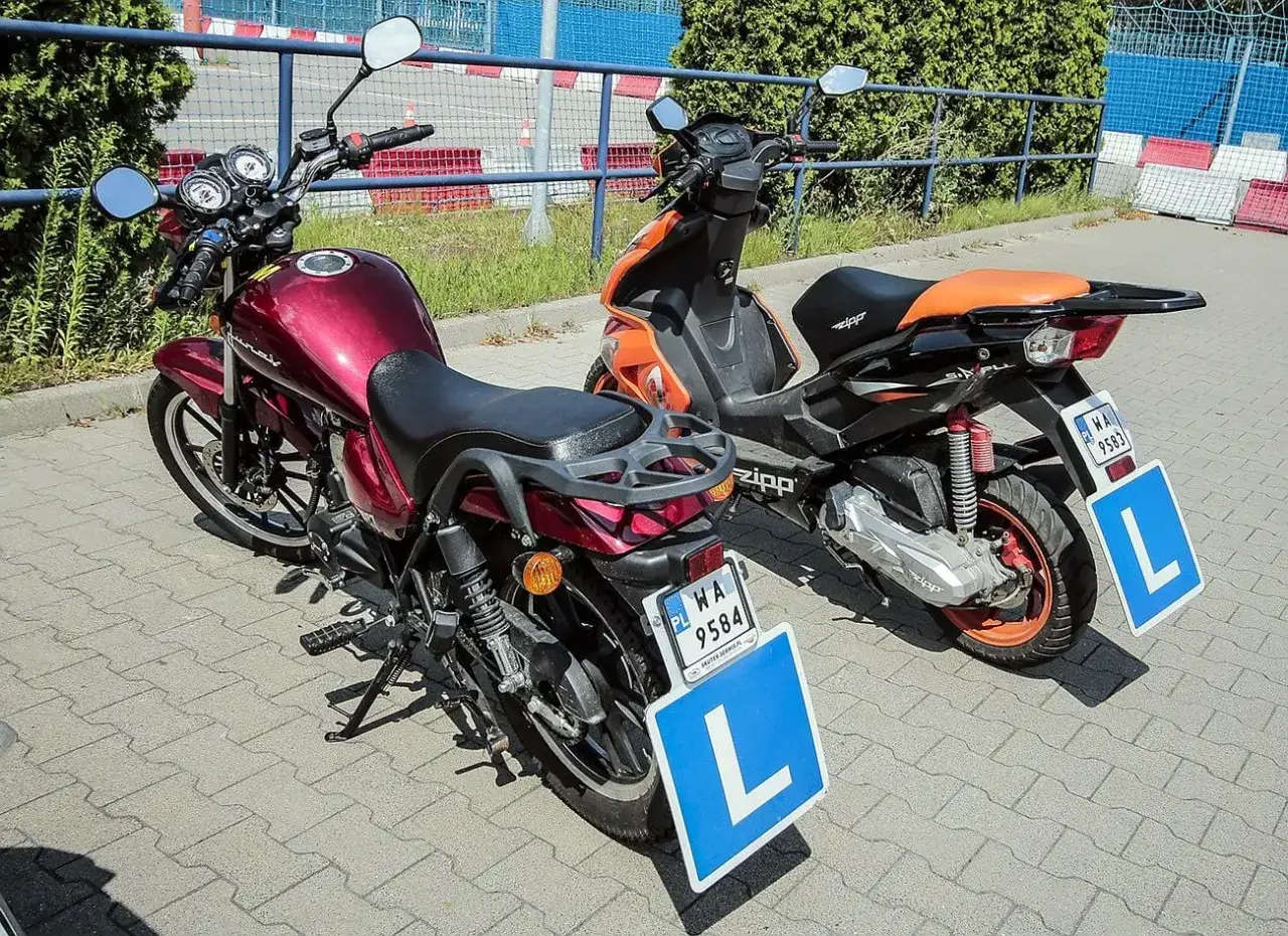Dwa motocykle, jeden czerwony, drugi pomarańczowy, z tabliczkami