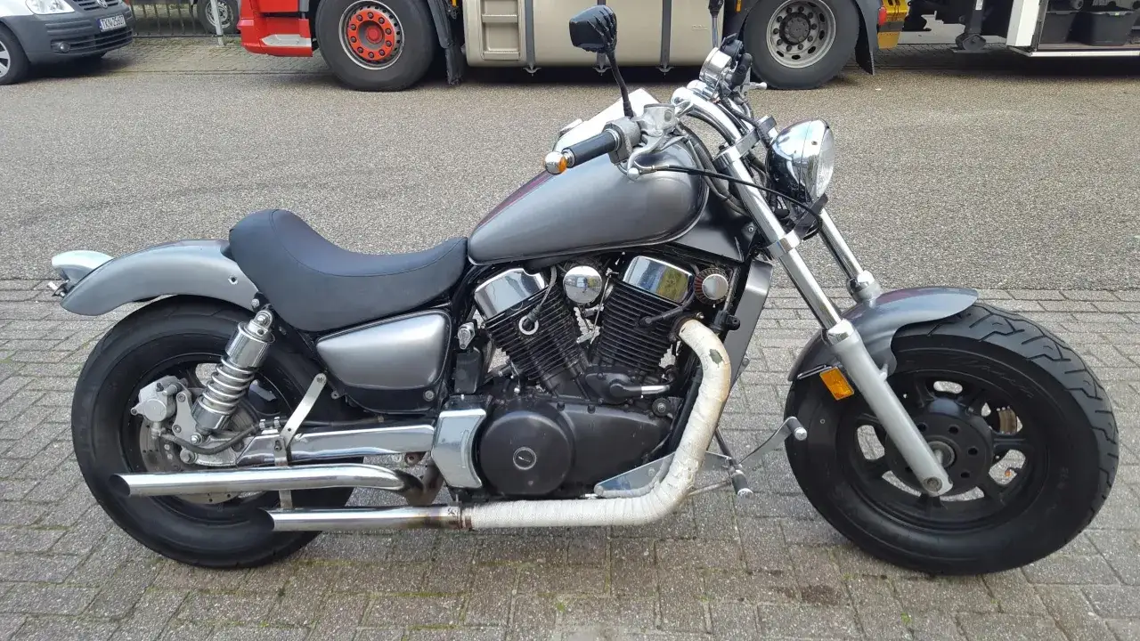 Szary Kawasaki Vulcan 1500, z widocznymi wadami wydechu i siedzenia, stoi na bruku.