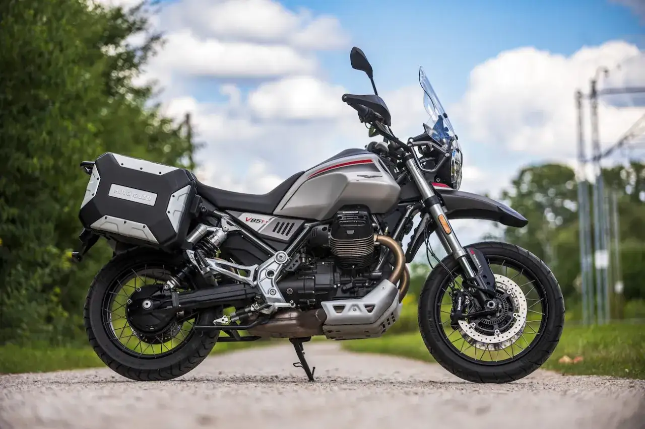 Srebrny motocykl Moto Guzzi V85 TT z kuframi, gotowy na przygodę na drodze i poza nią.