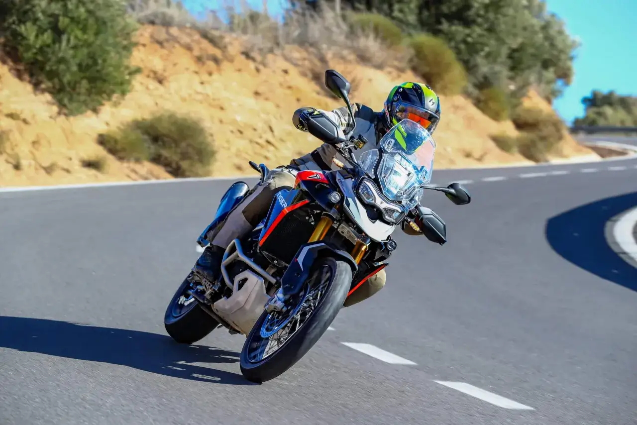 Motocyklista w kasku i stroju pokonuje zakręt na drodze na motocyklu Triumph Tiger 900 GT Pro.