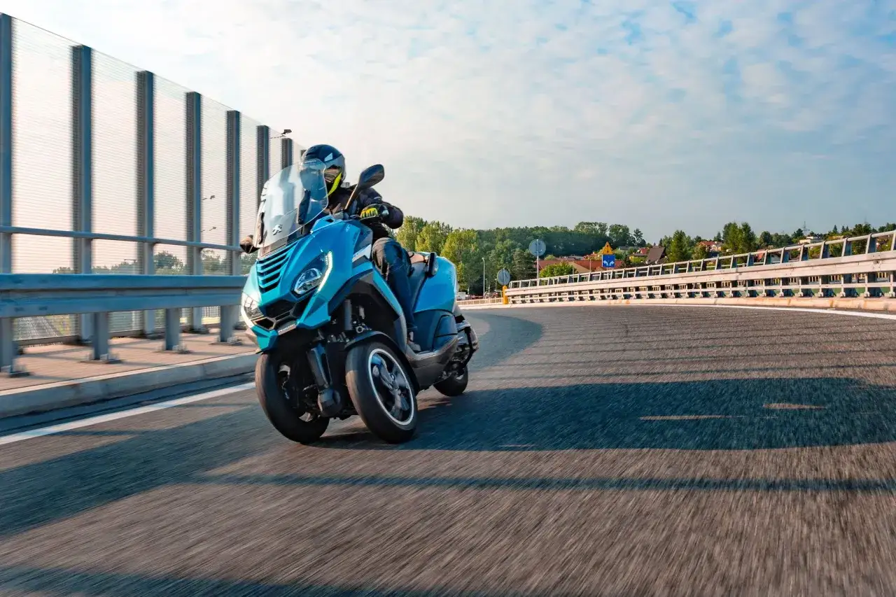 Jeżdżący na niebieskim trójkołowcu motocykliście, który zastanawia się, czy prawo jazdy kat B uprawnia do kierowania motorowerem.