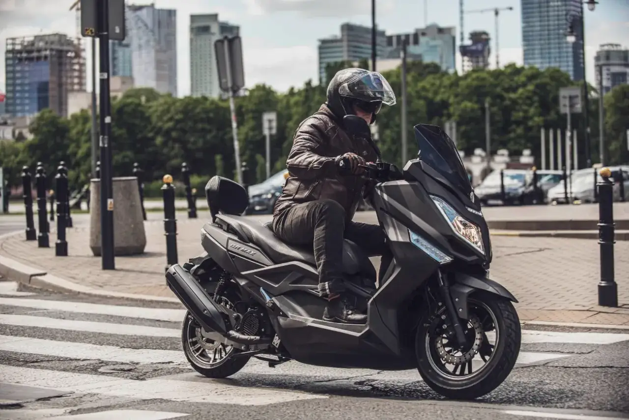 Mężczyzna w skórzanej kurtce jedzie na skuterze Zipp QR Max 125 przez miejskie przejście dla pieszych.