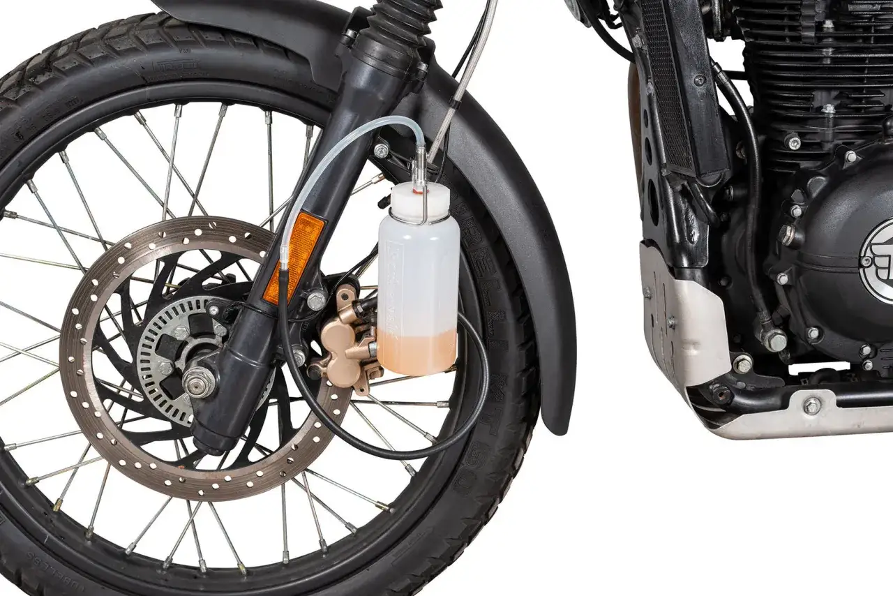Zestaw do odpowietrzania hamulców z ABS w motocyklu. Przezroczysty zbiorniczek z płynem podłączony do zacisku hamulcowego.