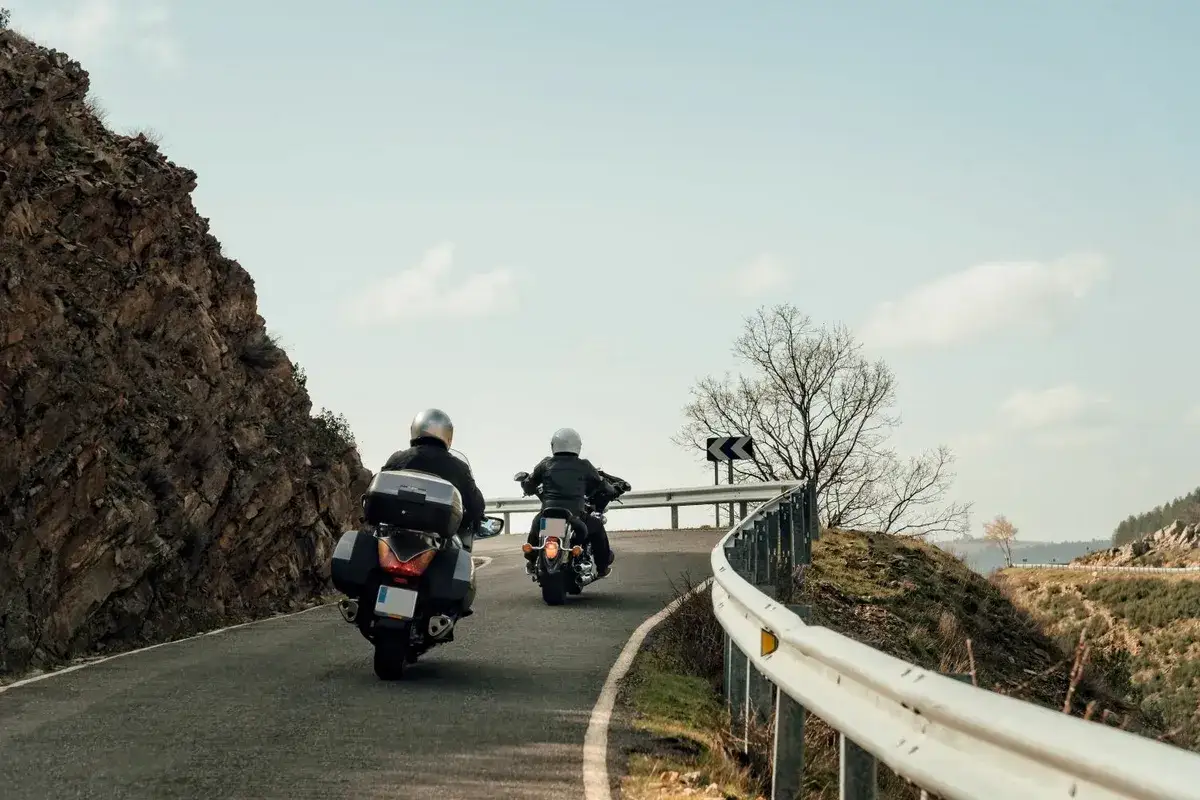 Dwaj motocykliści w kaskach jadą krętą drogą przez górzysty teren. Przygotowują się na wyprawę motocyklem dookoła Polski.