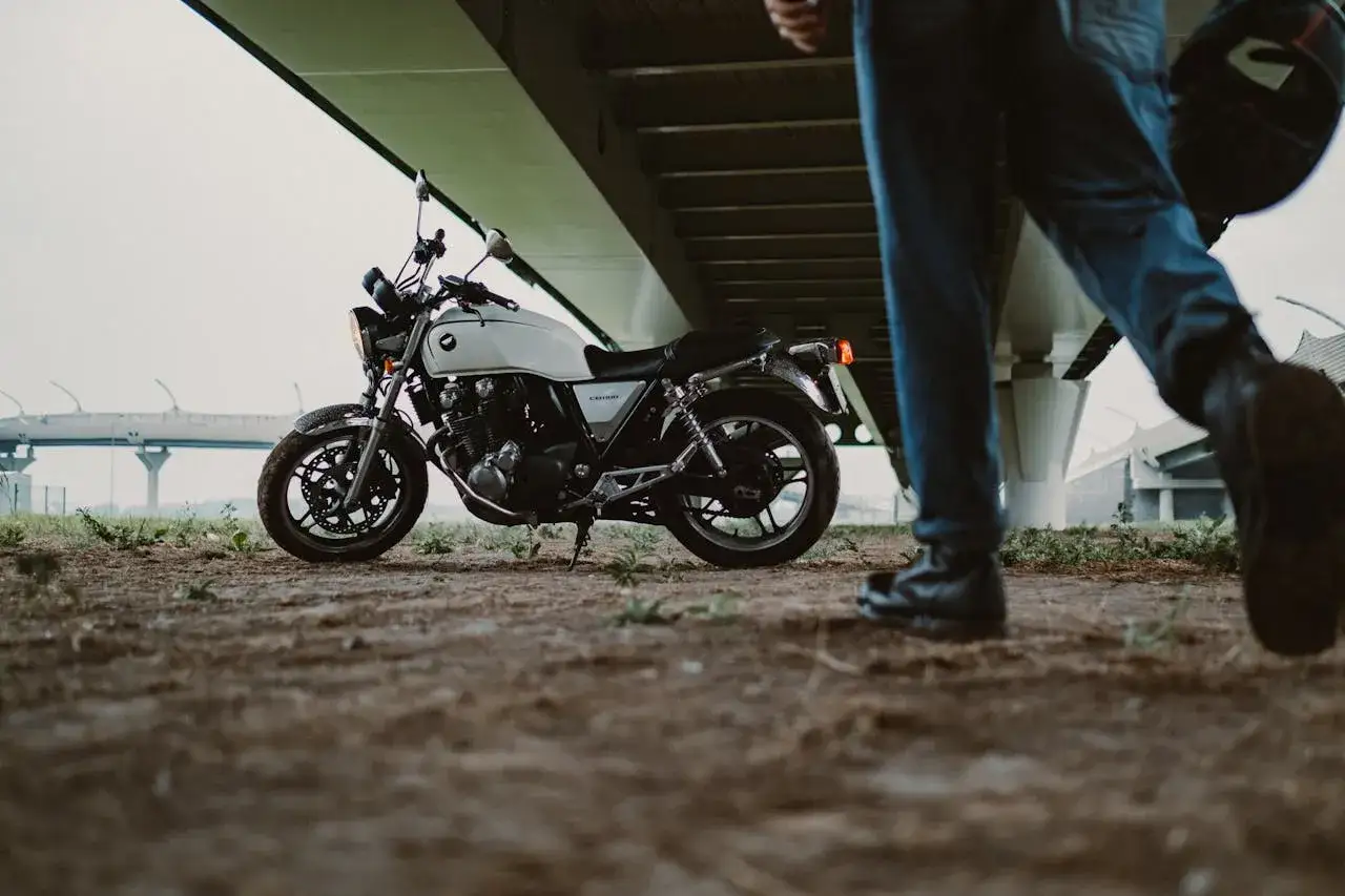 Biały motocykl czeka pod estakadą. Kierowca w jeansach i skórzanych butach, z kaskiem w ręku, rusza w stronę maszyny. Motocykle na A2 to wolność.