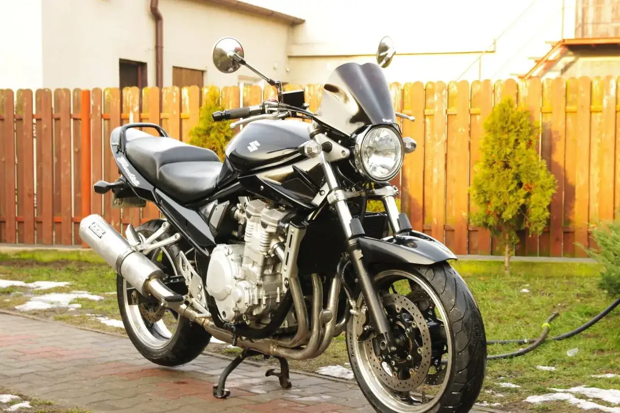 Czarny Suzuki Bandit 600, gotowy do jazdy, z mocą 77 KM, zaparkowany przy drewnianym płocie.