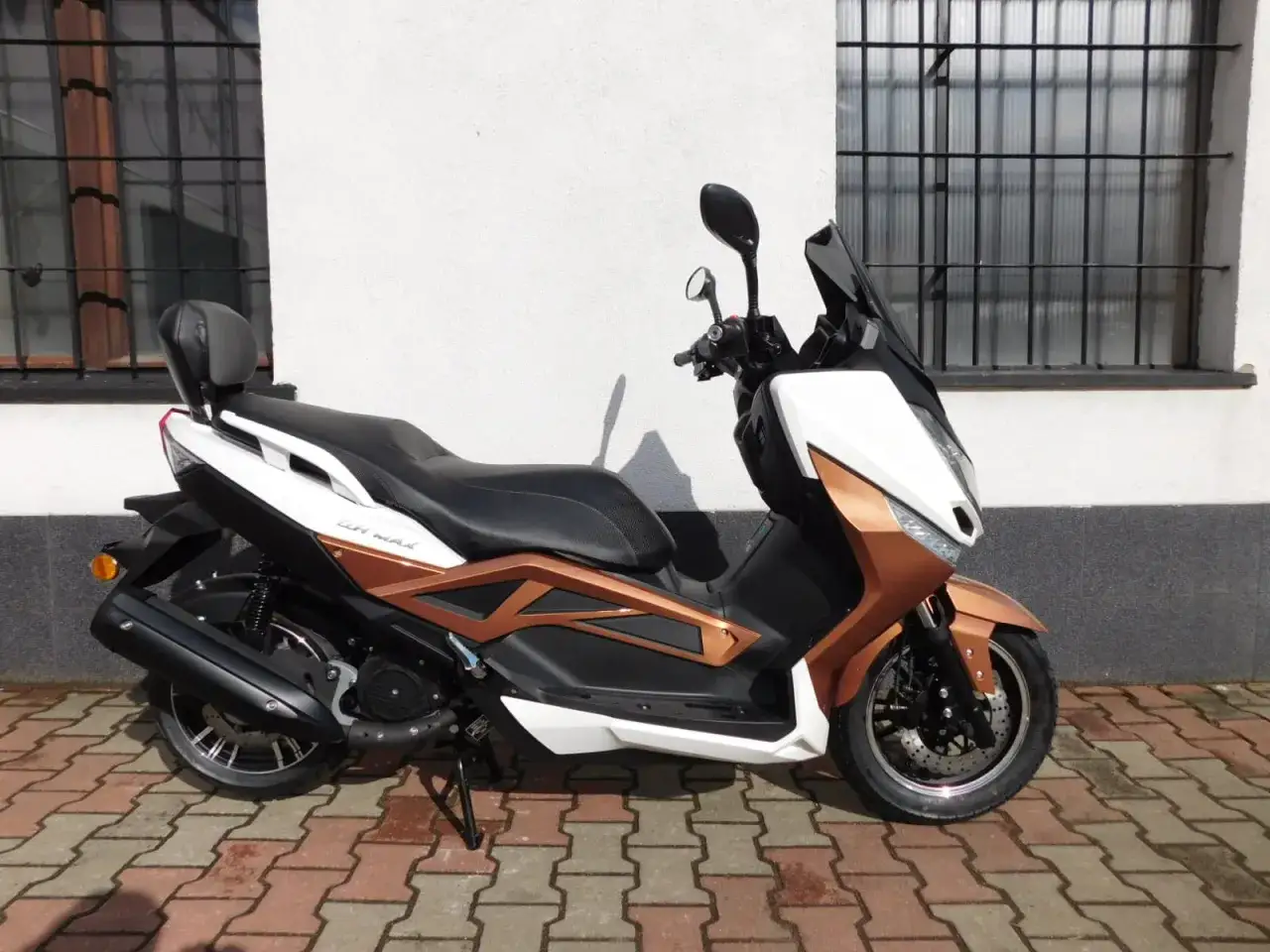 Nowy skuter Zipp QR Max 125 w kolorze miedziano-białym, zaparkowany na chodniku z kostki brukowej.